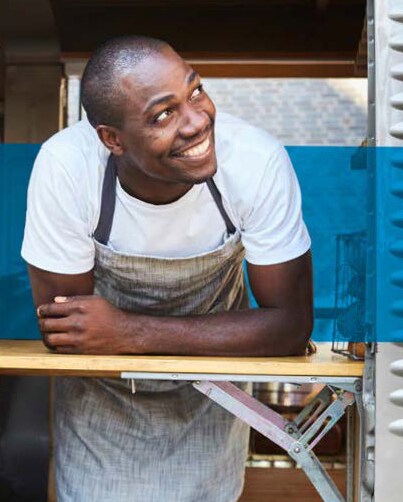man in apron leaning out food truck window smiling