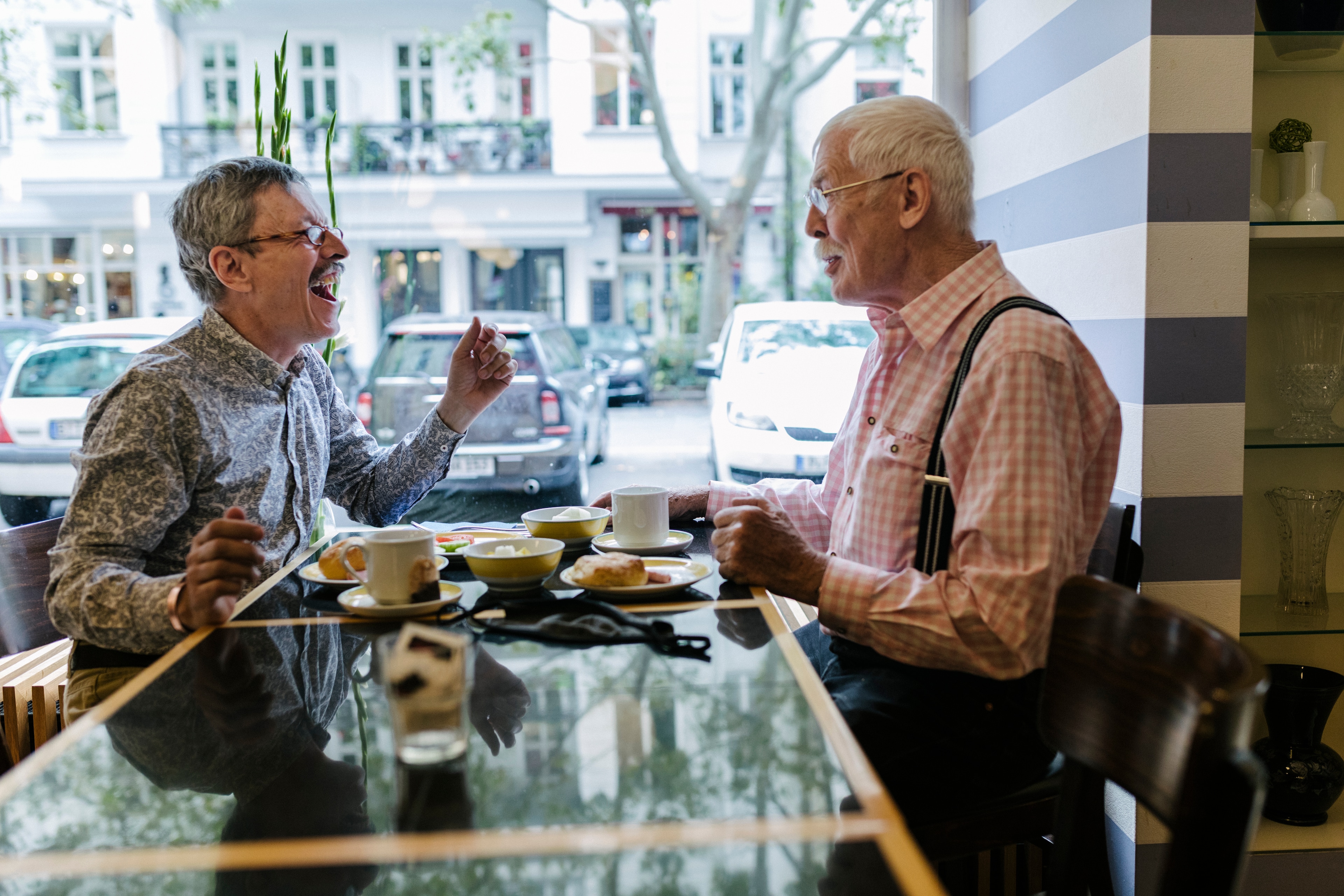 Two retired men laugh together at a cafe