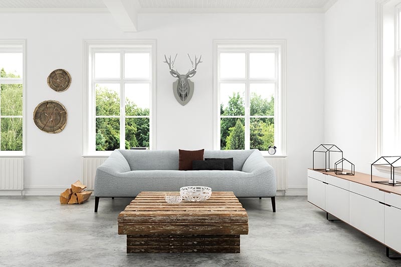 white walled living room with a gray couch, a low wooden table and a gray wooden cardboard deer head mount on the wall