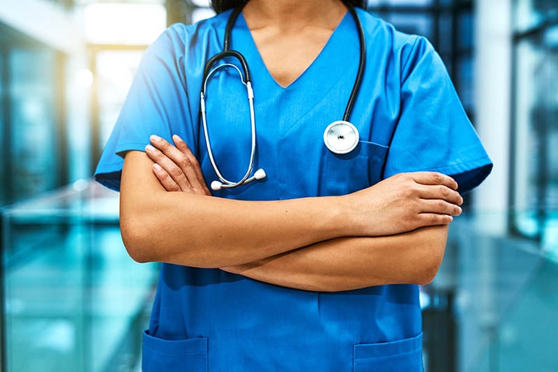 unidentifiable nurse in blue scrubs with crossed arms and a stethoscope