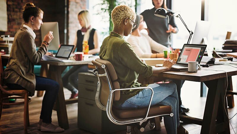 woman with short hair in a green shirt sits at a desk in a shared coworking space