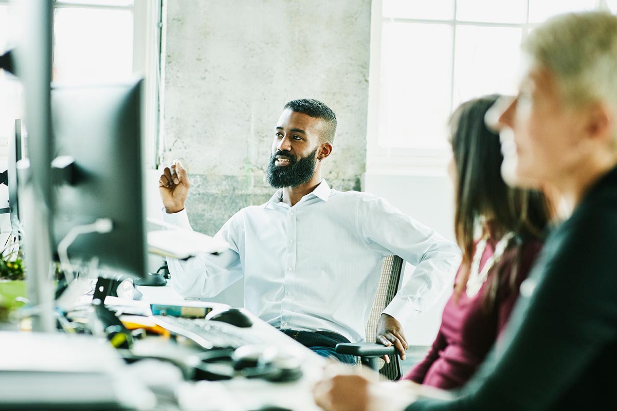 A man at his computer discusses with coworkers