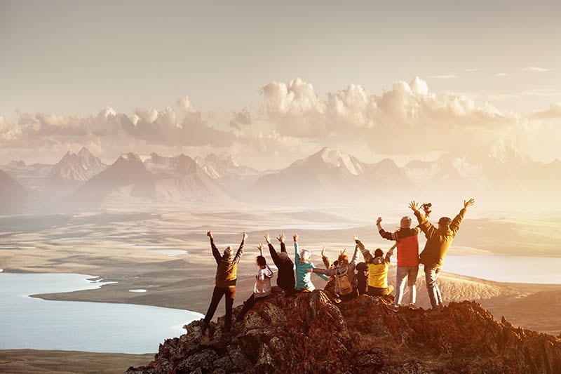 a group of friends celebrate with their hands in the air at the top of a mountain