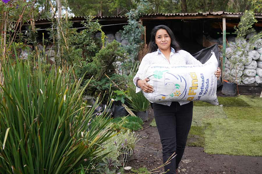 Elizabeth Flores carries a large bag of planting soil
