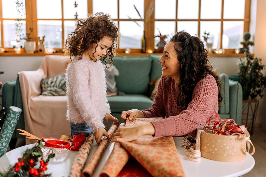 A mother and daughter wrap gifts in festive paper