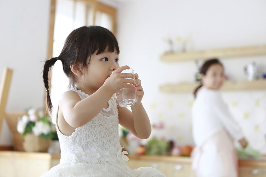 A young girl drinks a glass of water in a kitchen