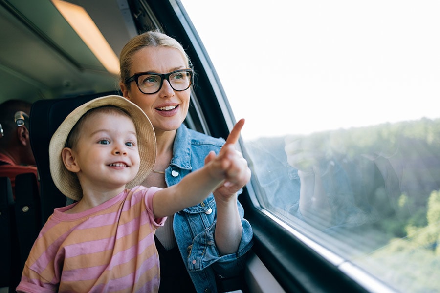A small child sits on her mother's lap and looks out the window of a train