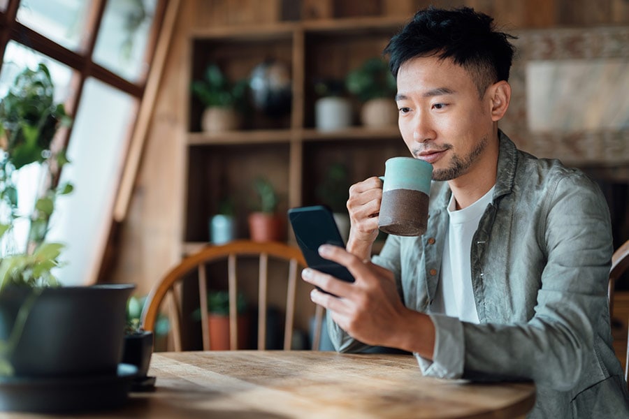 A man checks his investments on a phone while drinking his morning coffee