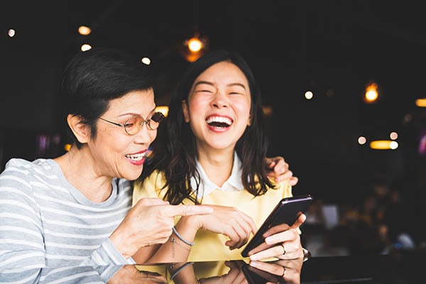 Asian mother and daughter laughing while looking at a mobile phone