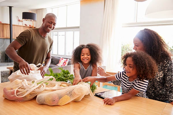 Family returning home from shopping trip unpacking plastic free grocery bags
