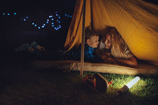 mother and son in a backyard tent at night smiling at each other 